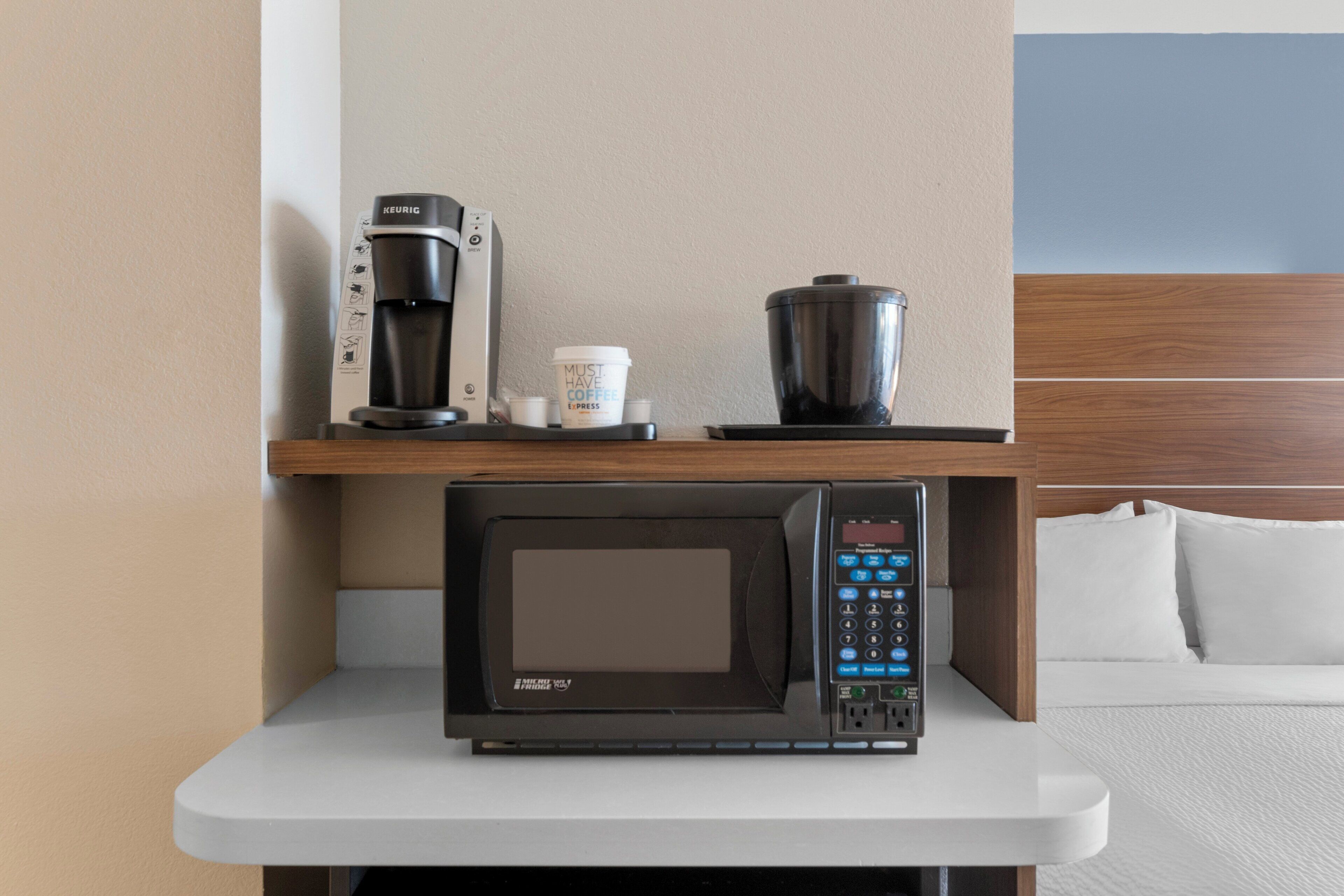 A compact kitchenette with a coffee maker, a coffee cup, and a microwave on a white countertop.