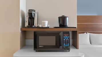 Une petite cuisine équipée comprenant une machine à café, une tasse à café et un four à micro-ondes, le tout posé sur un plan de travail blanc.