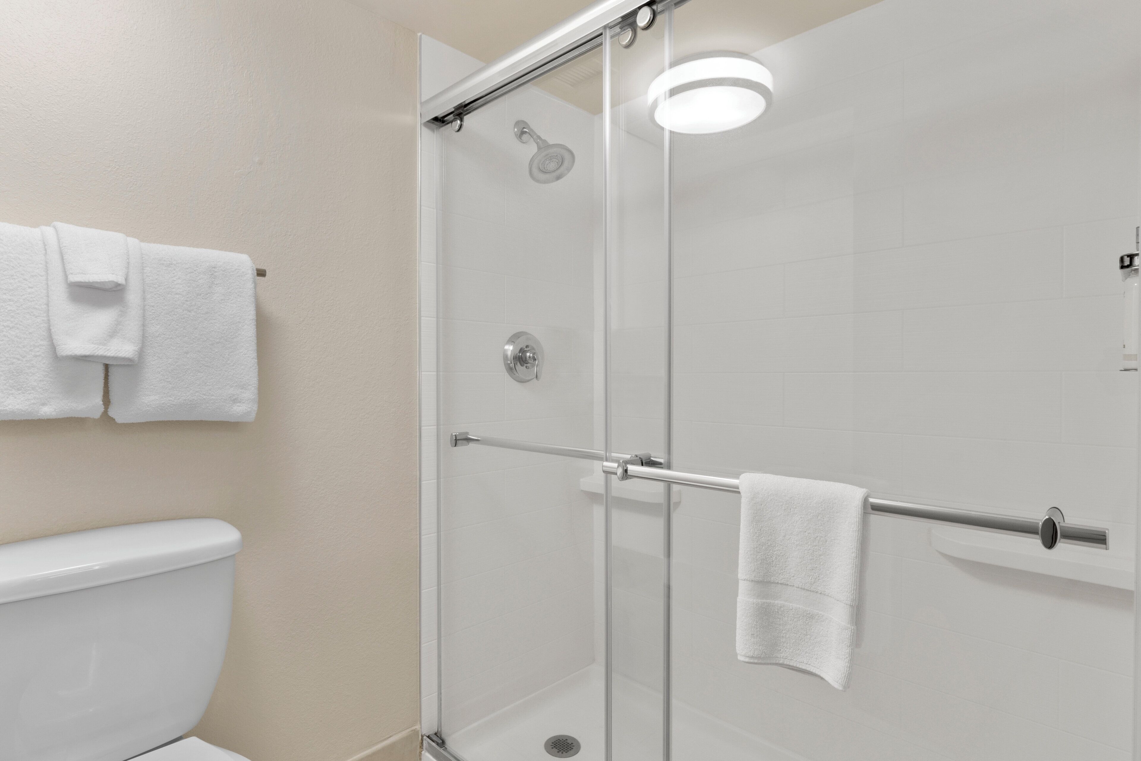 A modern bathroom with a glass shower enclosure, a toilet, and a towel rack with two towels.