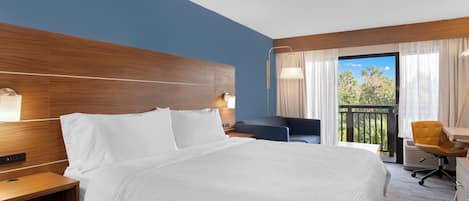 Habitación de hotel con una cama grande, un escritorio, una silla y un balcón con cortinas.