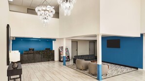 A modern lobby with a reception desk, a chandelier, a blue accent wall, and a seating area with a patterned rug.