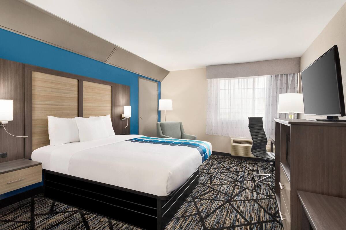 A hotel room with a large bed, a desk, a chair, a television, and a window with curtains.
