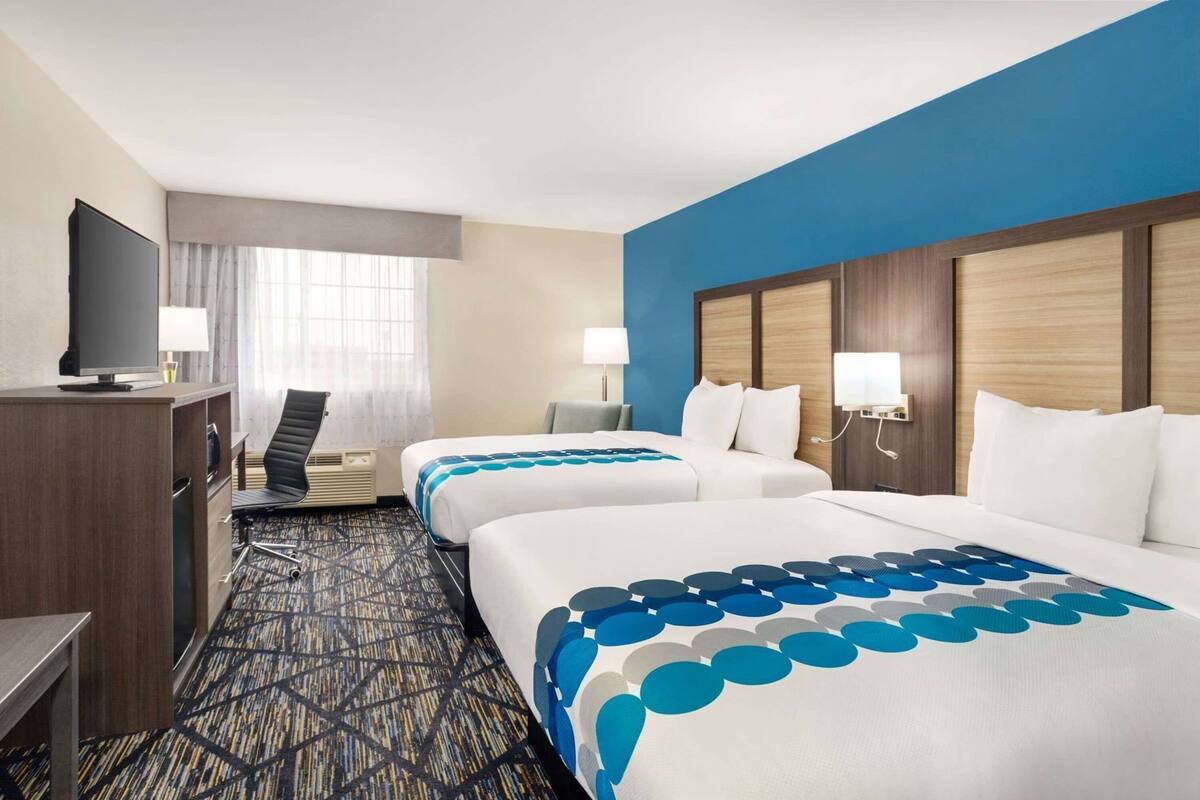 A hotel room with two beds, a desk, a television, and a window with curtains.