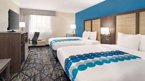 A hotel room with two beds, a desk, a TV, and a window with curtains.