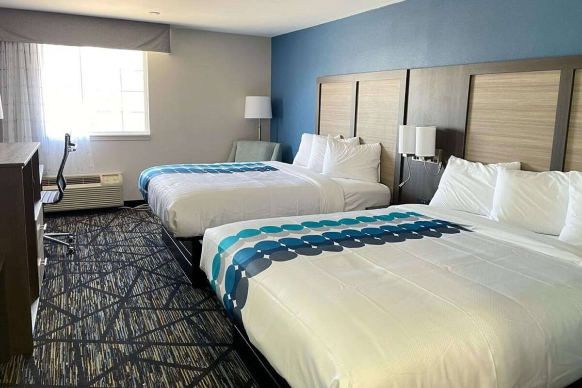 A hotel room with two beds, a desk, a chair, a lamp, and a window.