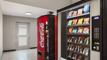 En automattillbehörsmaskin med snacks och en läskautomat med Coca-Cola-produkter, placerade i en korridor.