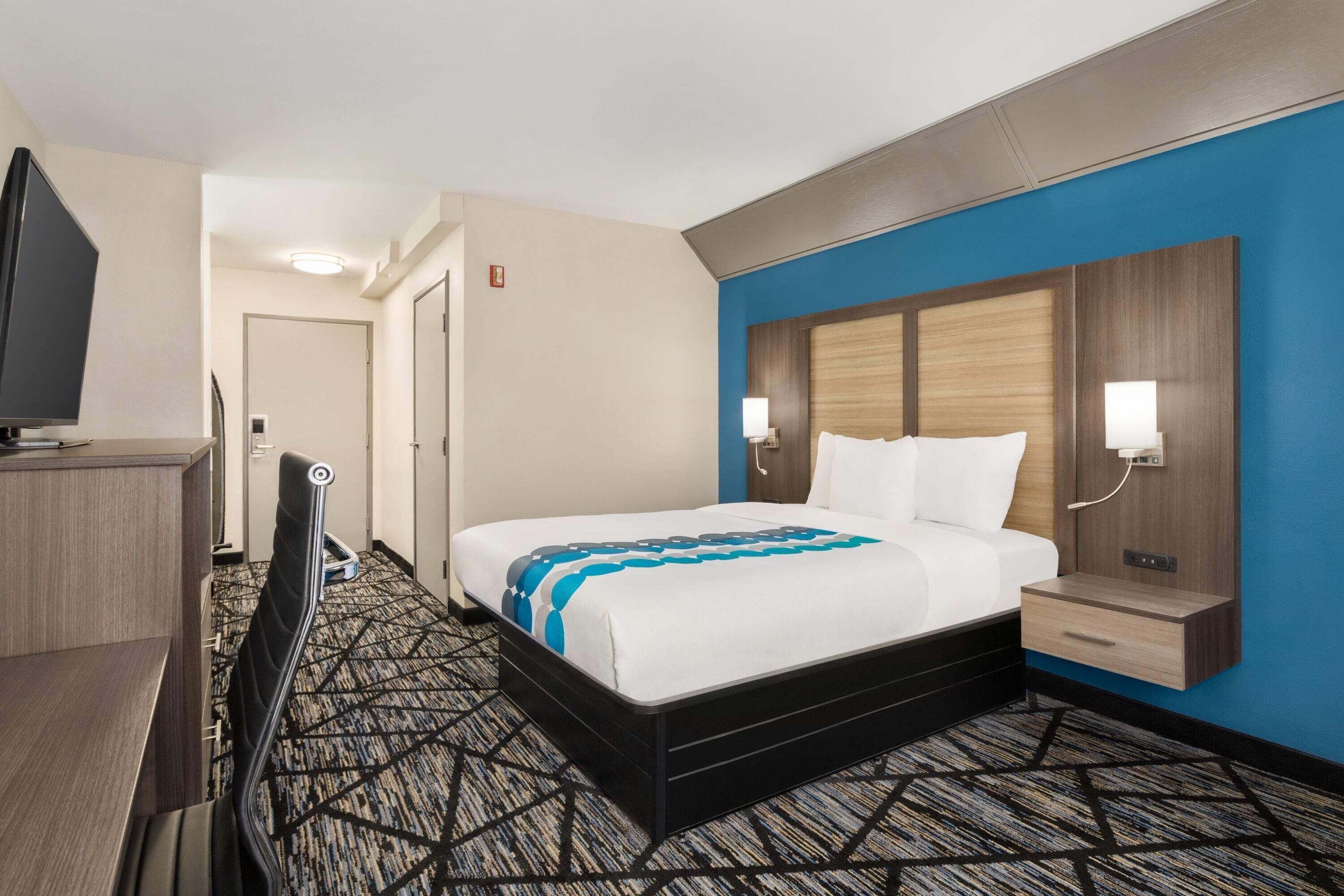 A hotel room with a bed, bedside tables, a desk, and a TV.