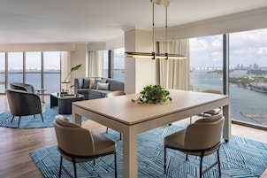 A modern living room with a dining area, large windows, and a view of the city and water.