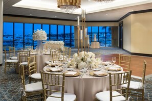 A banquet hall with round tables set for a formal event, featuring gold chairs and white tablecloths.