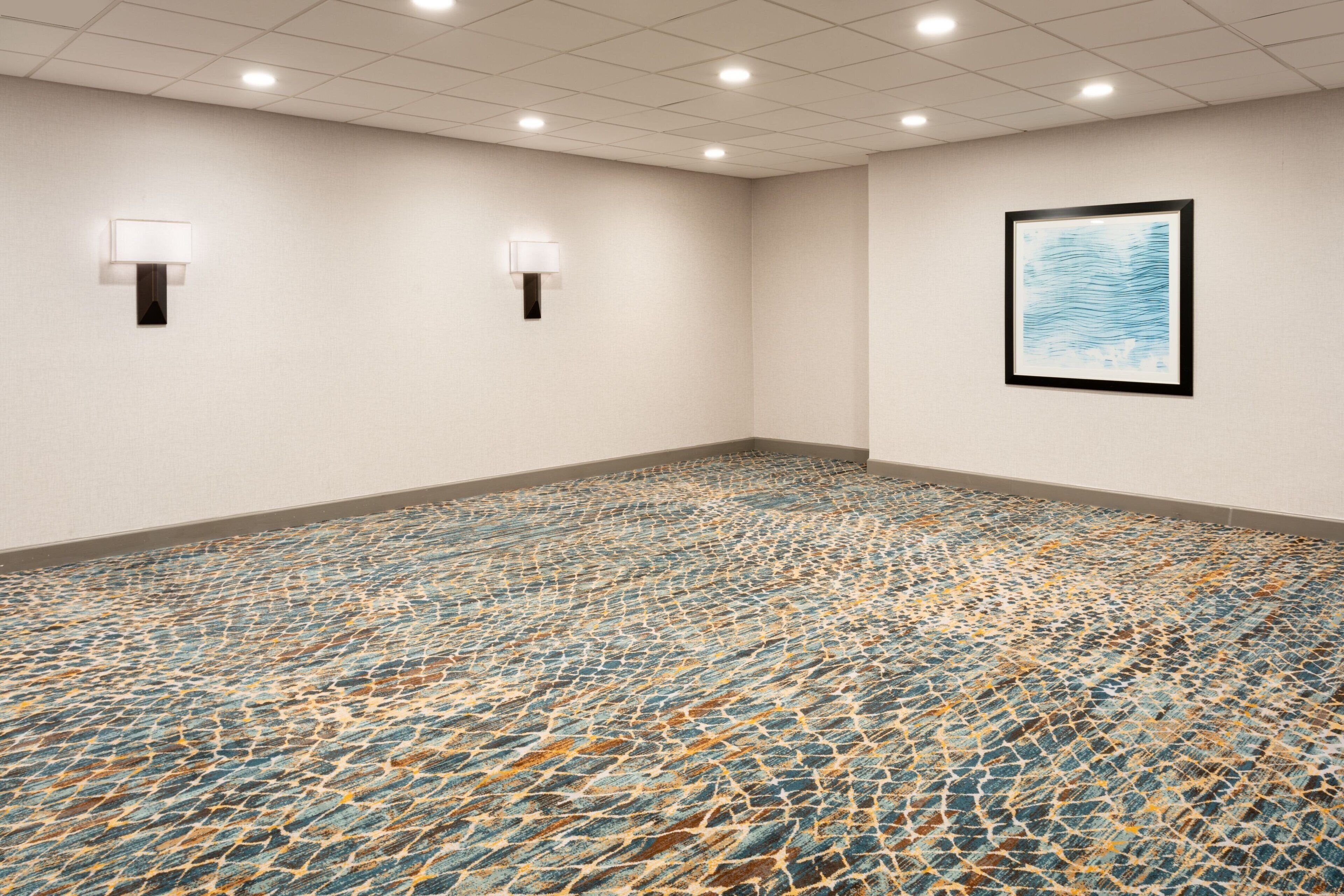A conference room with a patterned carpet, two wall-mounted lamps, and a framed artwork on the wall.