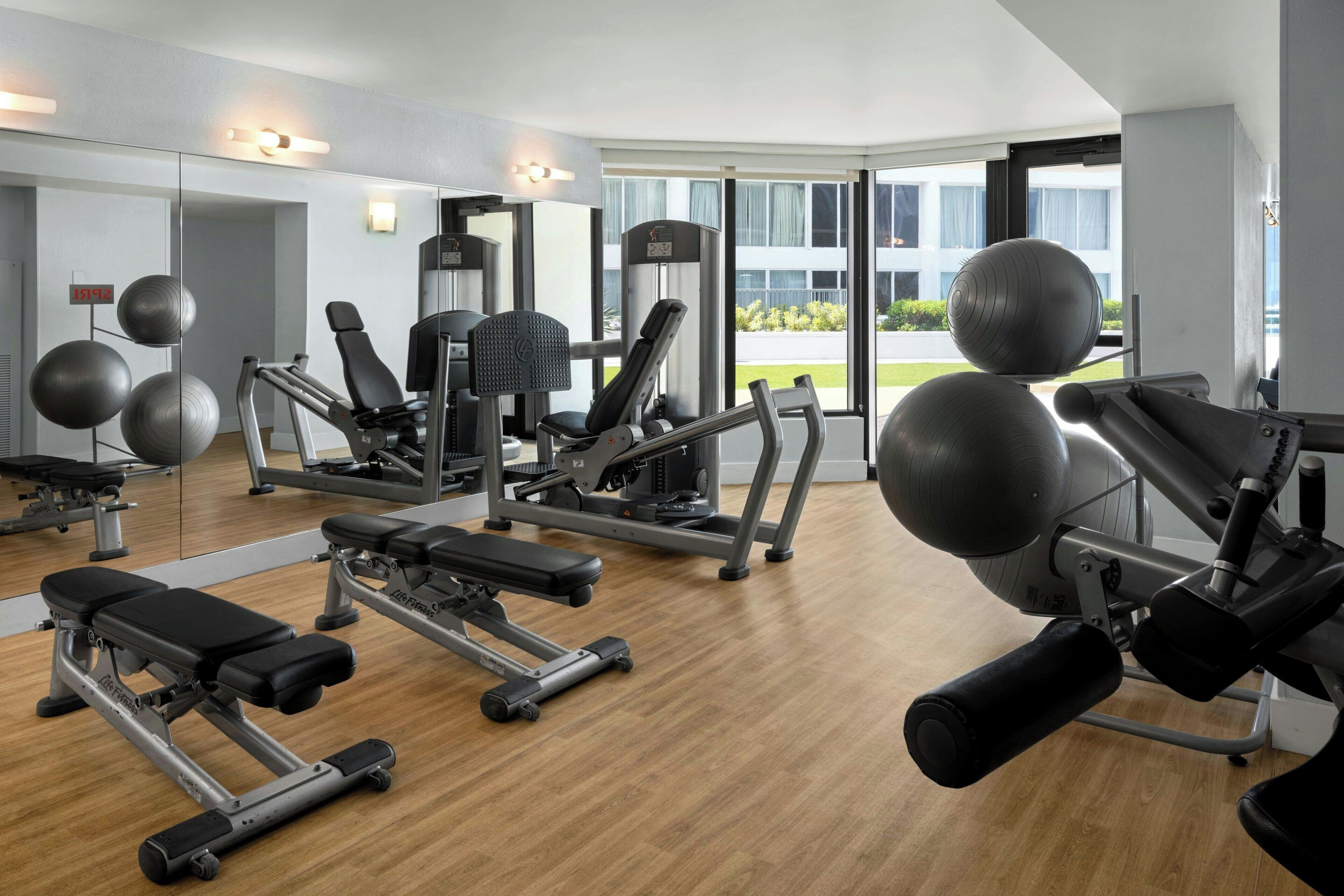 A gym with various exercise equipment, large windows, and a view of the outdoors.