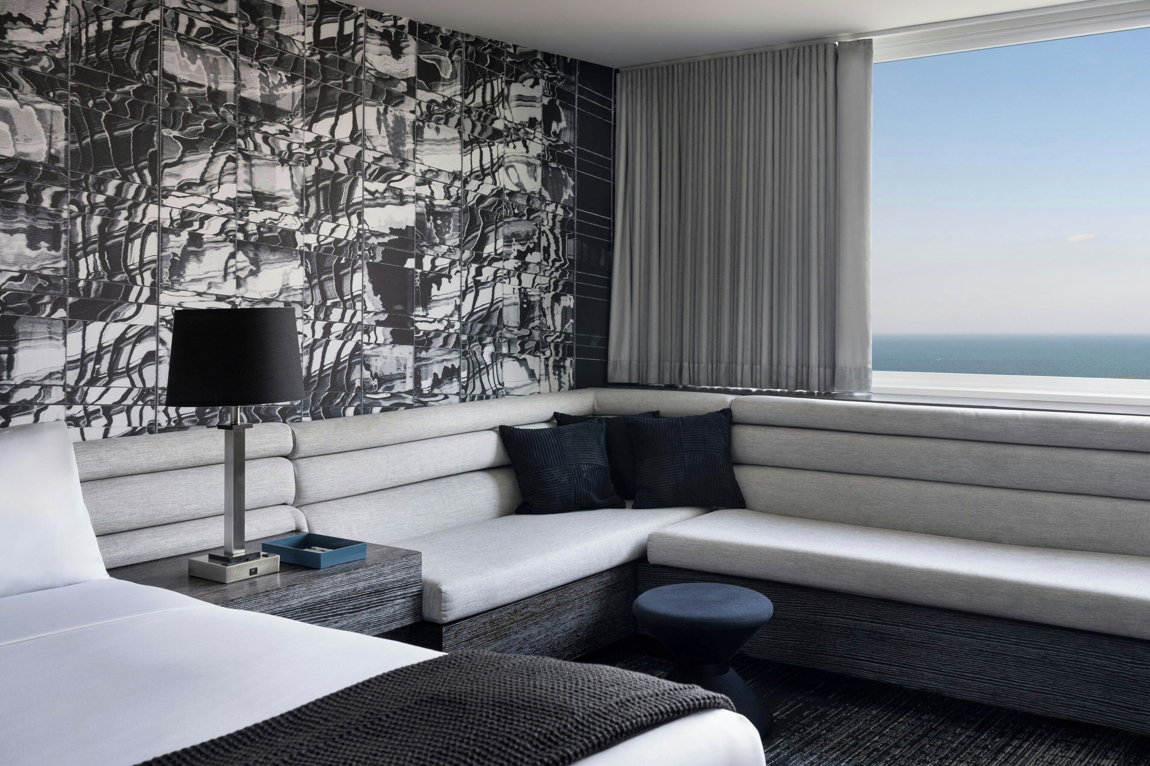 Une chambre d'hôtel moderne avec une grande fenêtre, un canapé, un lit et un mur décoré d'un motif.