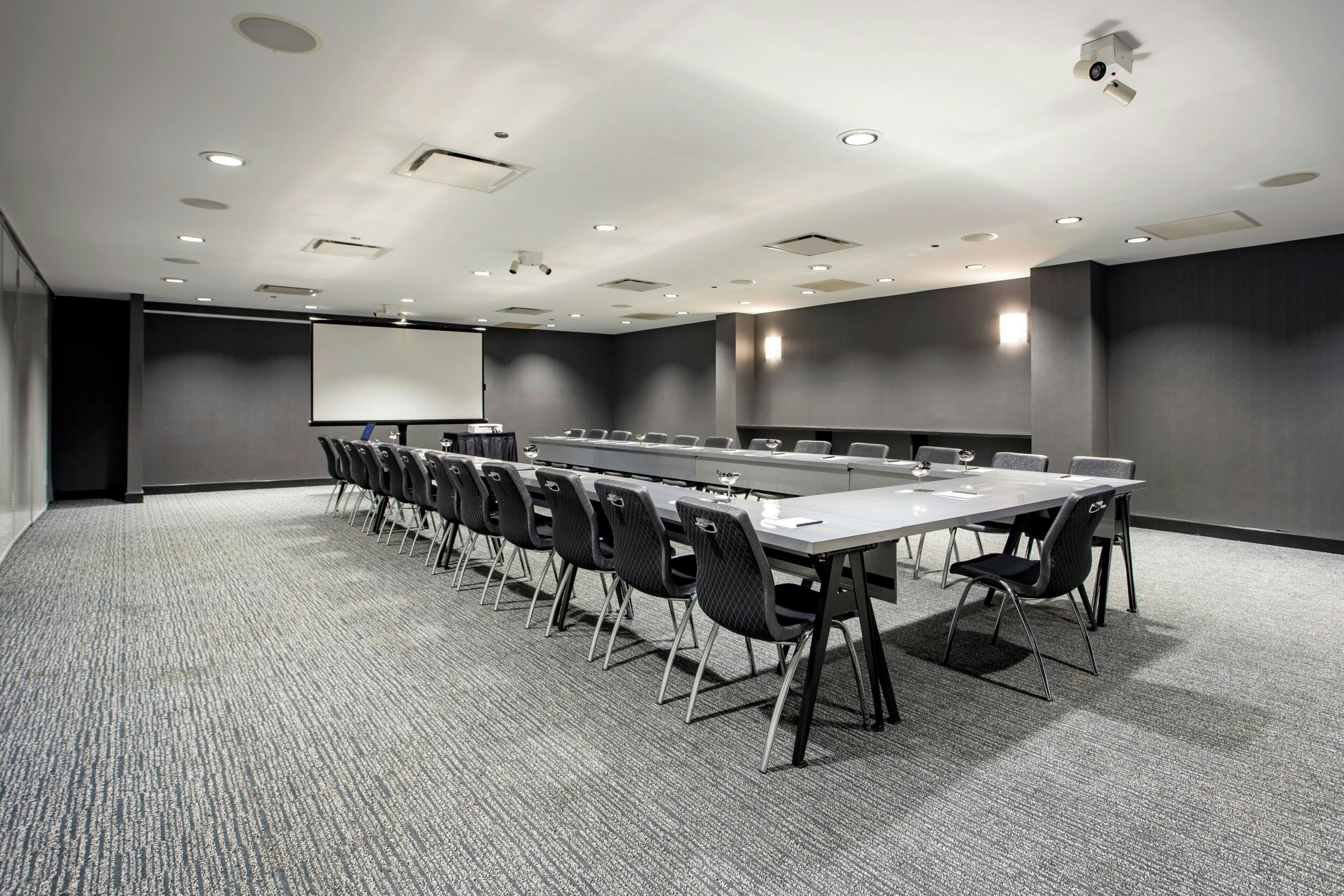 A conference room with a long table, chairs, a projector screen, and a carpeted floor.
