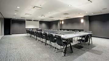 A conference room with a long table, chairs, a projector screen, and a carpeted floor.