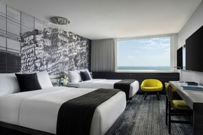 Ein Hotelzimmer mit zwei Betten, einem Schreibtisch, einem Stuhl, einem großen Fenster mit Blick und einem modernen Wanddesign.
