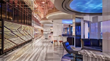 A modern hotel lobby with a marble floor, a seating area with a bar, and a unique ceiling design.