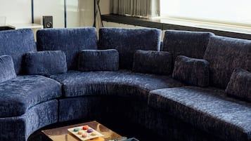 A modern living room with a sectional sofa, a coffee table with snacks, a lamp, and a large window with curtains.