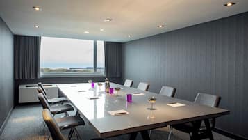 A conference room with a long table, chairs, and a view through large windows.