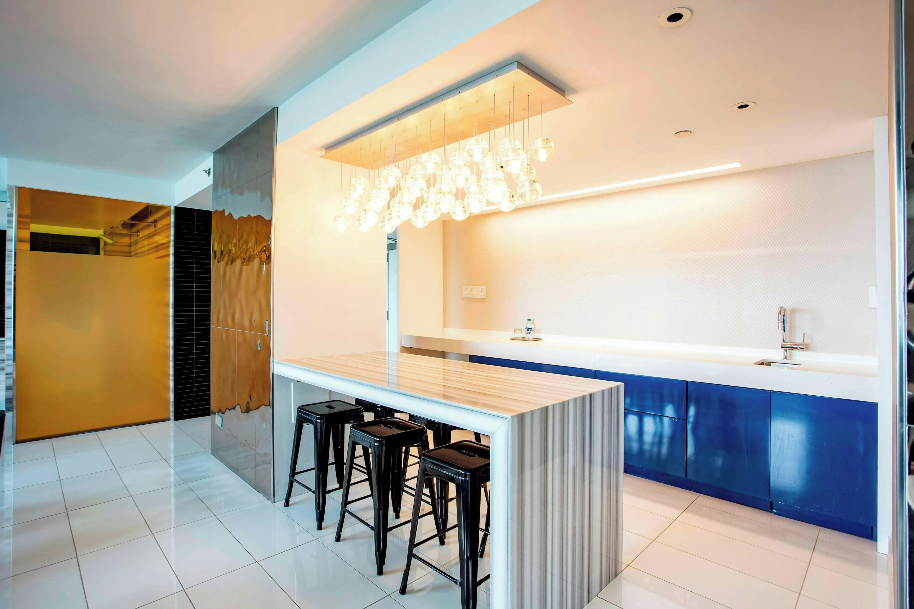 A modern kitchen with a central island, bar stools, a built-in sink, and a decorative light fixture.