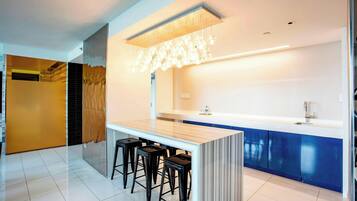 A modern kitchen with a central island, bar stools, a built-in sink, and a decorative light fixture.