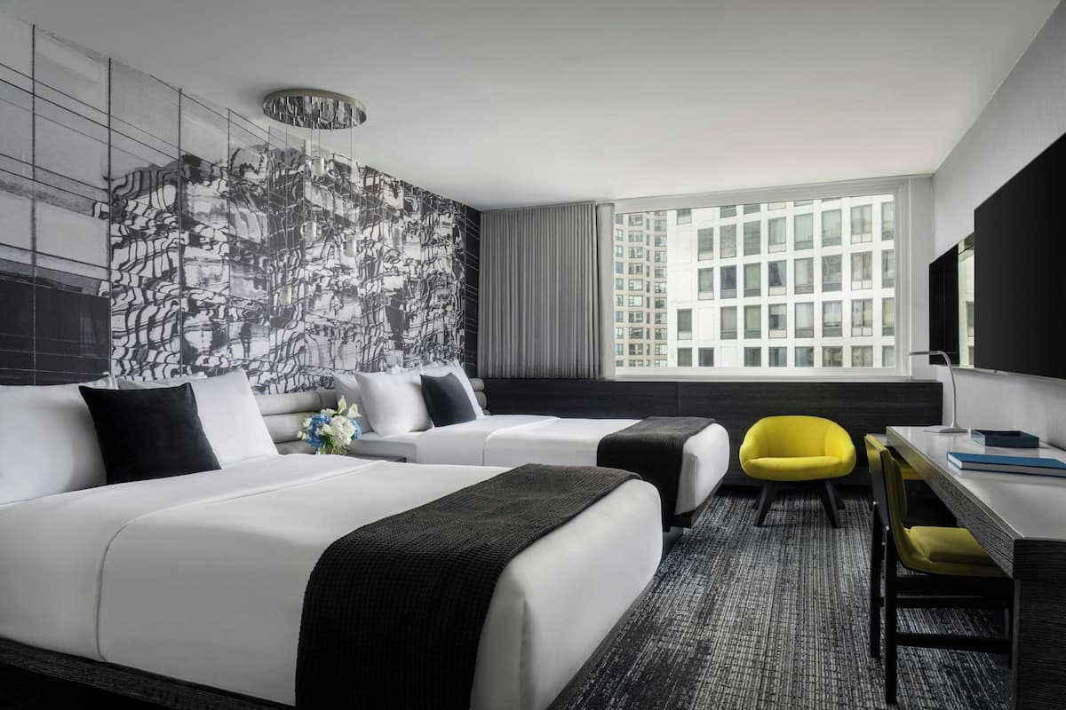 Une chambre d’hôtel avec deux lits, un bureau, une chaise et une grande fenêtre donnant sur la ville.