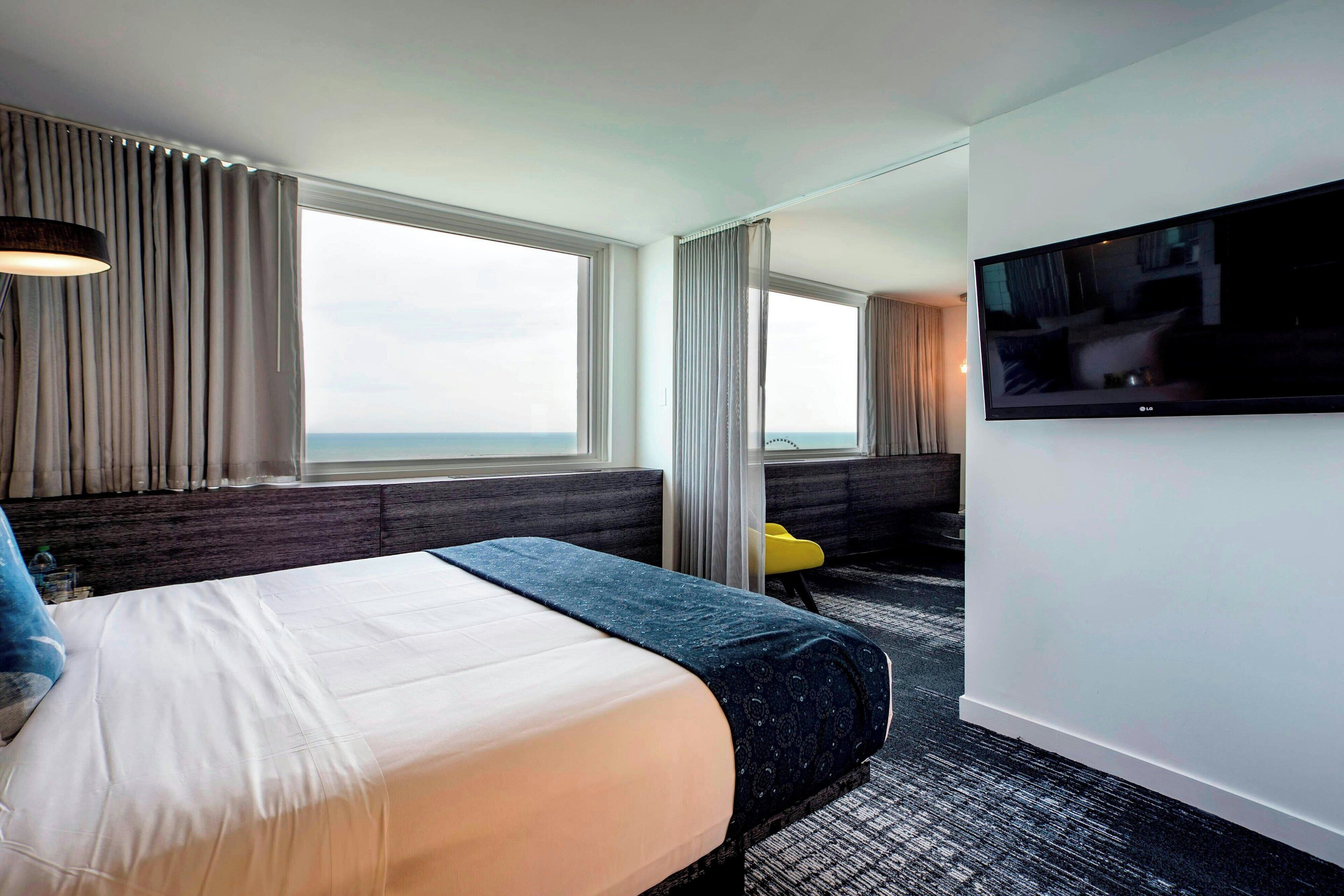 A hotel room with a bed, a TV, a desk, and a view of the sea.