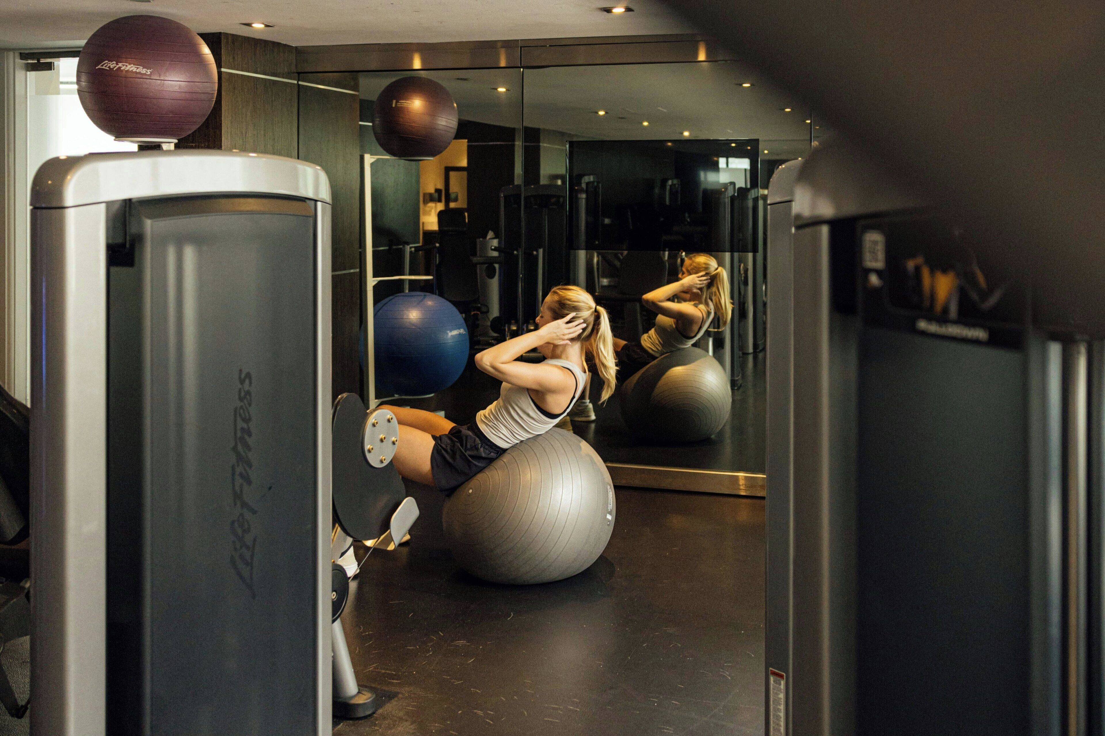 A gym with exercise equipment, including a mirrored wall and a large exercise ball.