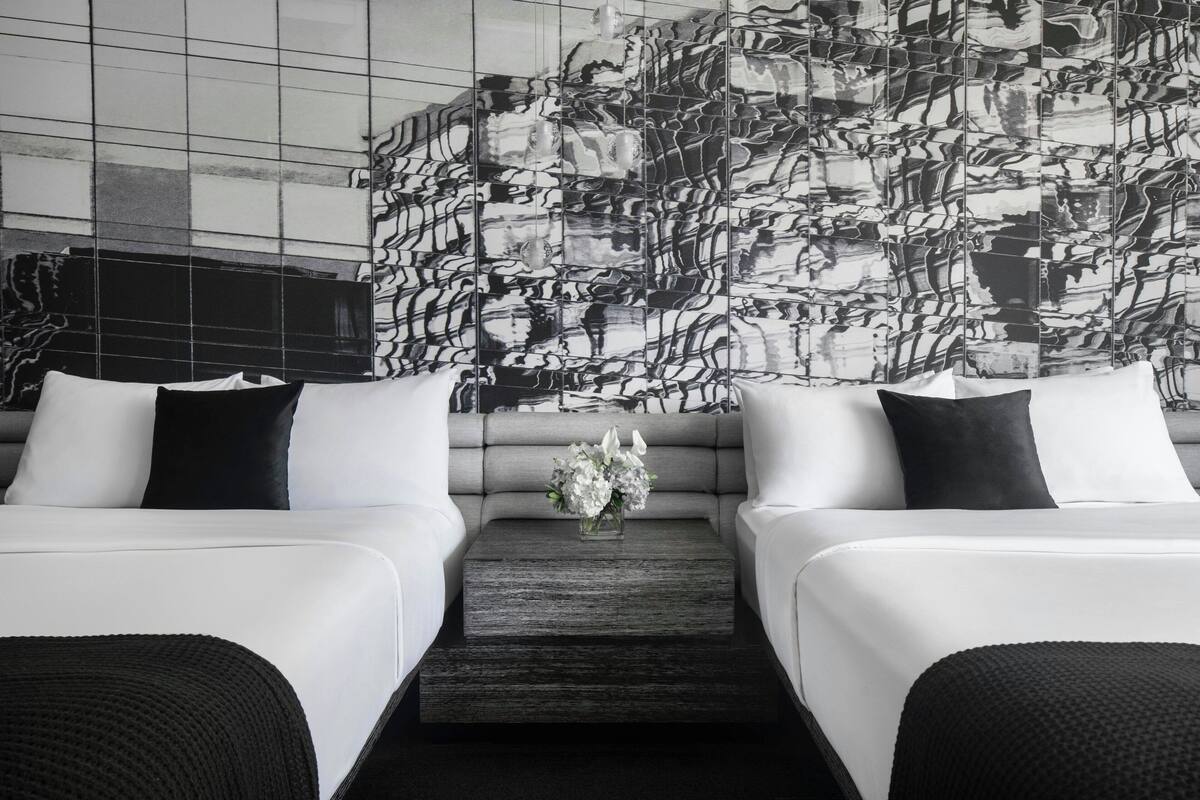 Une chambre d’hôtel moderne avec deux lits, une table basse en bois foncé et un grand tableau abstrait accroché au mur.