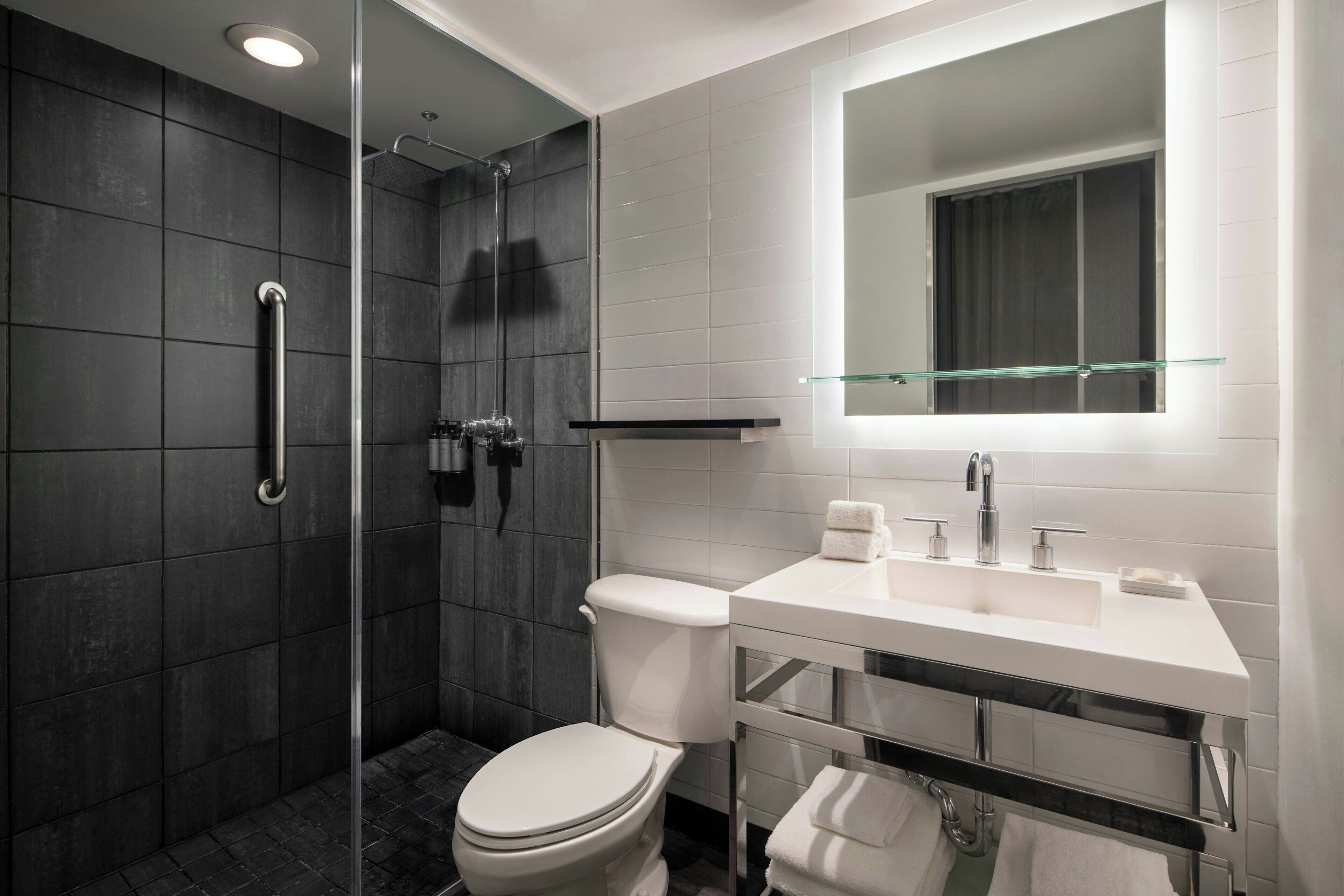 Une salle de bain moderne avec une douche à parois de verre, des toilettes blanches et un meuble-lavabo surmonté d’un miroir.