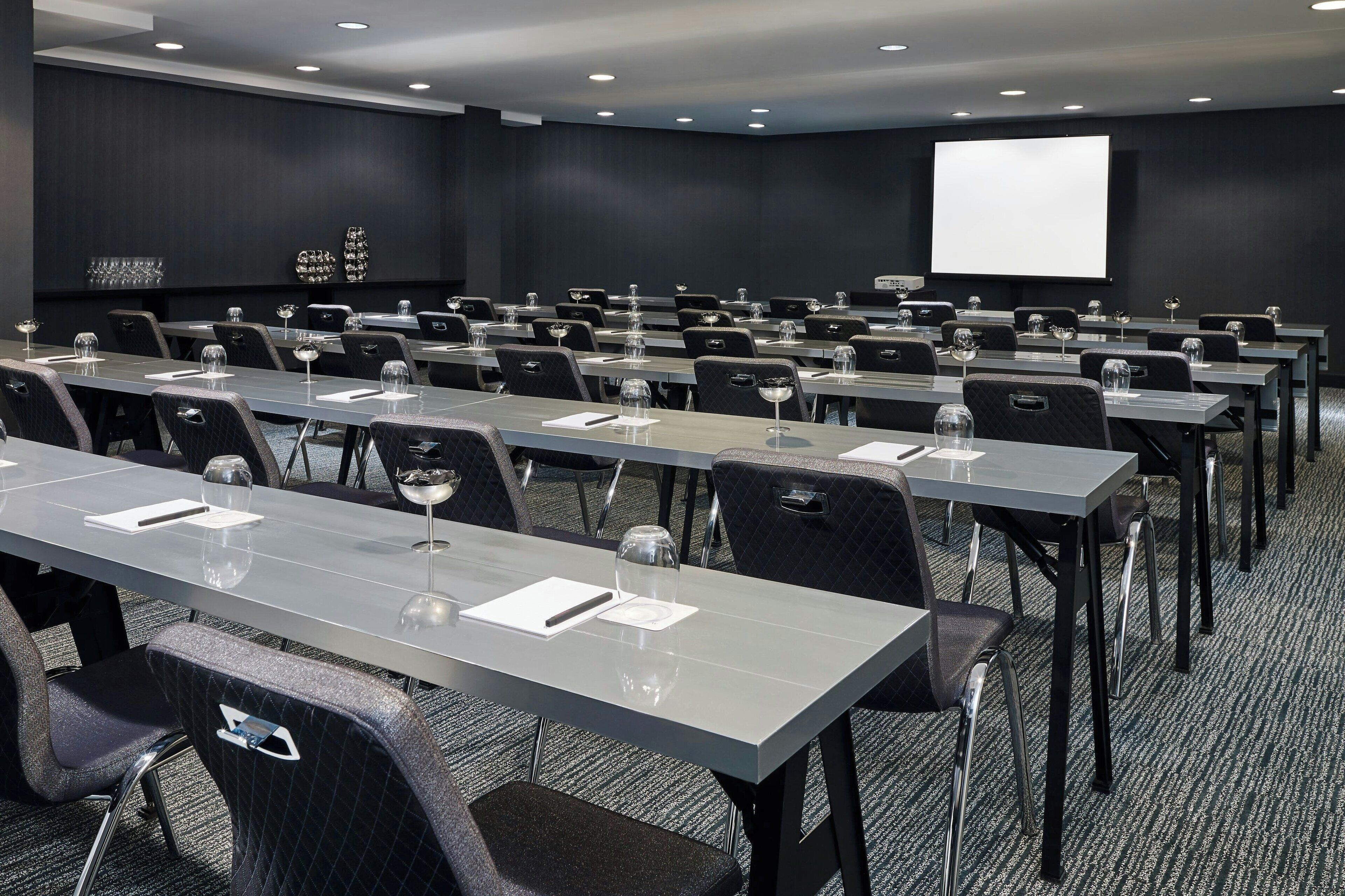 Une salle de conférence dotée de plusieurs tables et de chaises, ainsi que de verres à eau et de porte-noms.