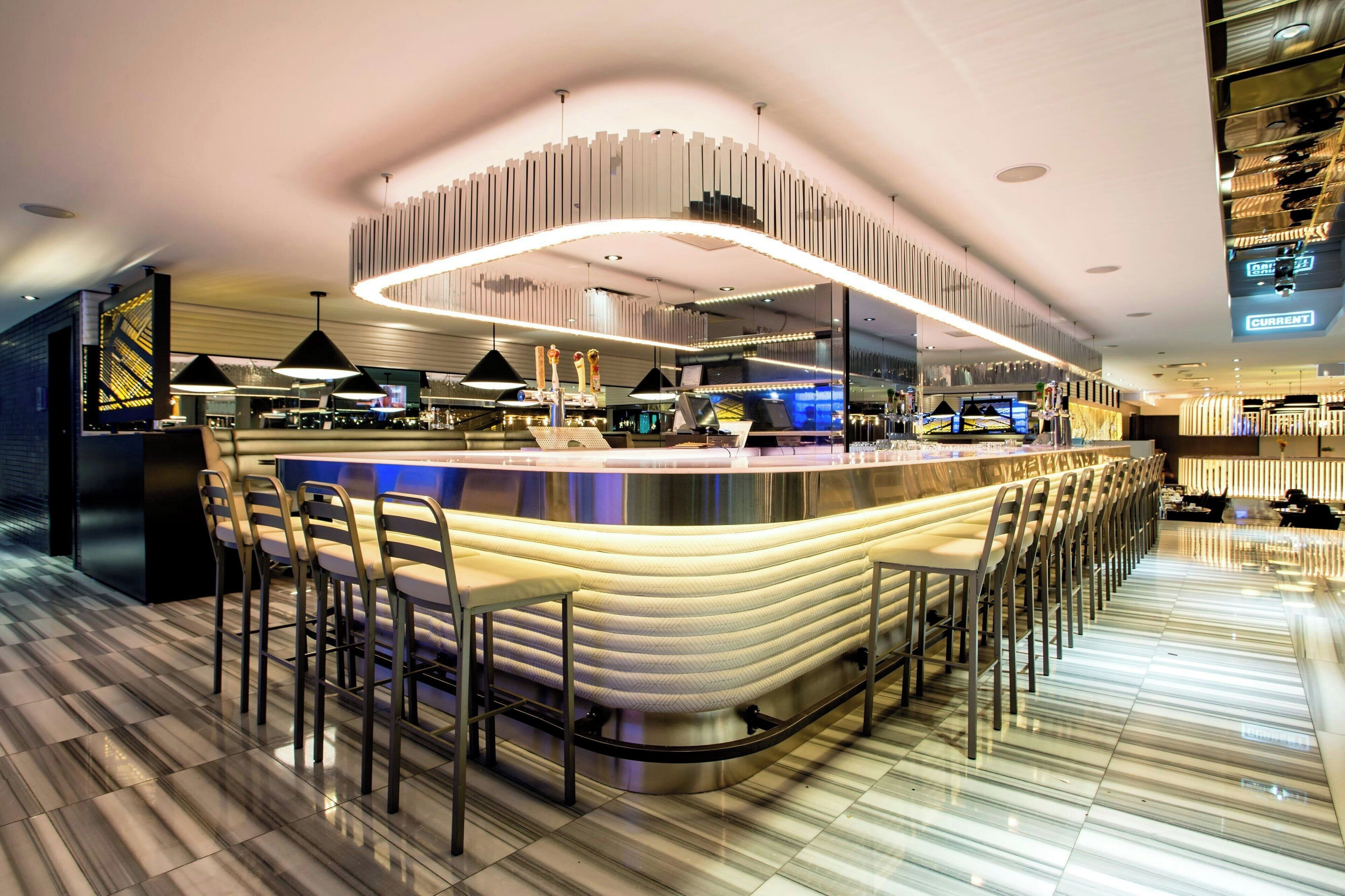 A modern bar area with a curved counter, multiple bar stools, and pendant lighting.