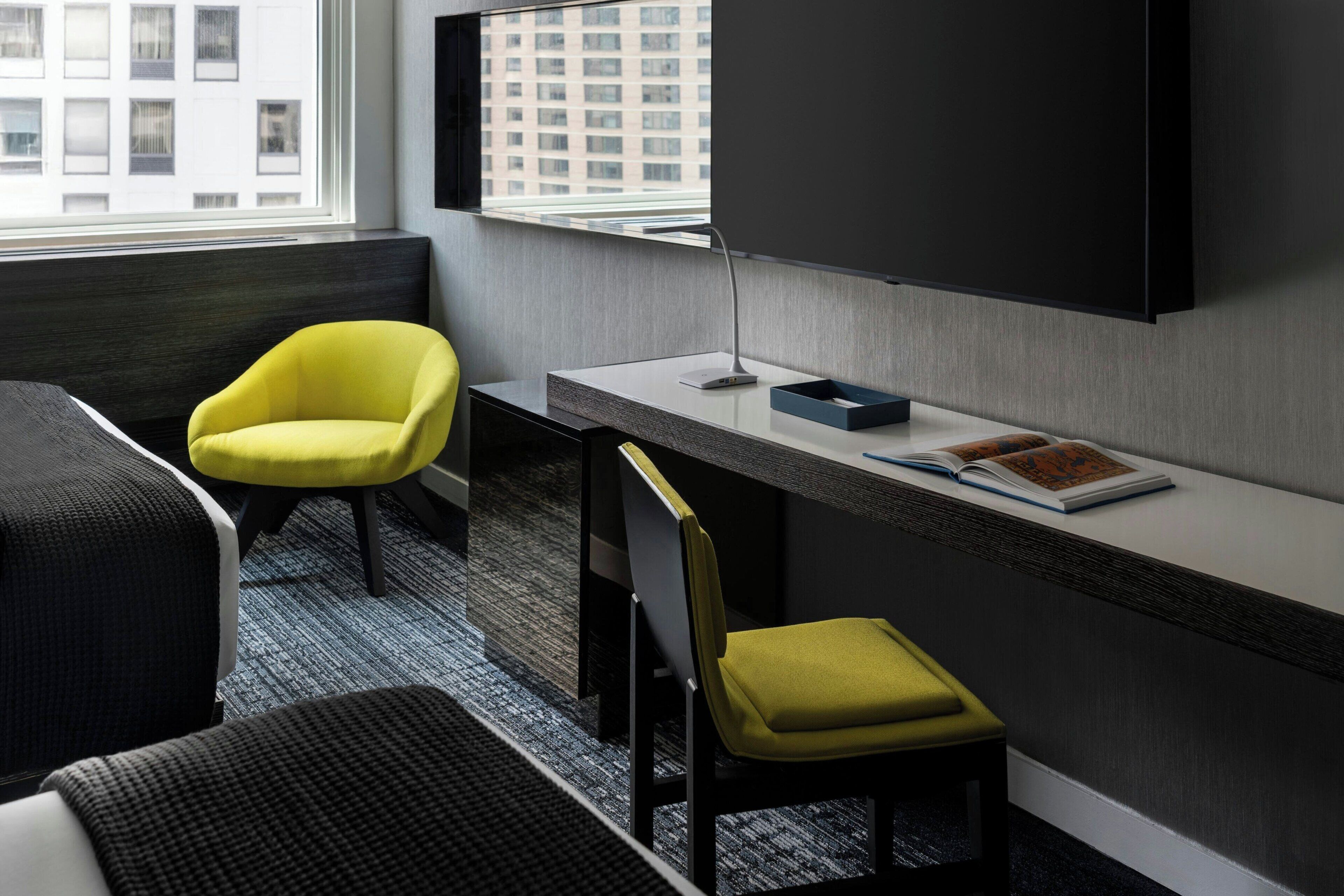 Een moderne hotelkamer met een bed, een bureau, een stoel en een televisie aan de muur.