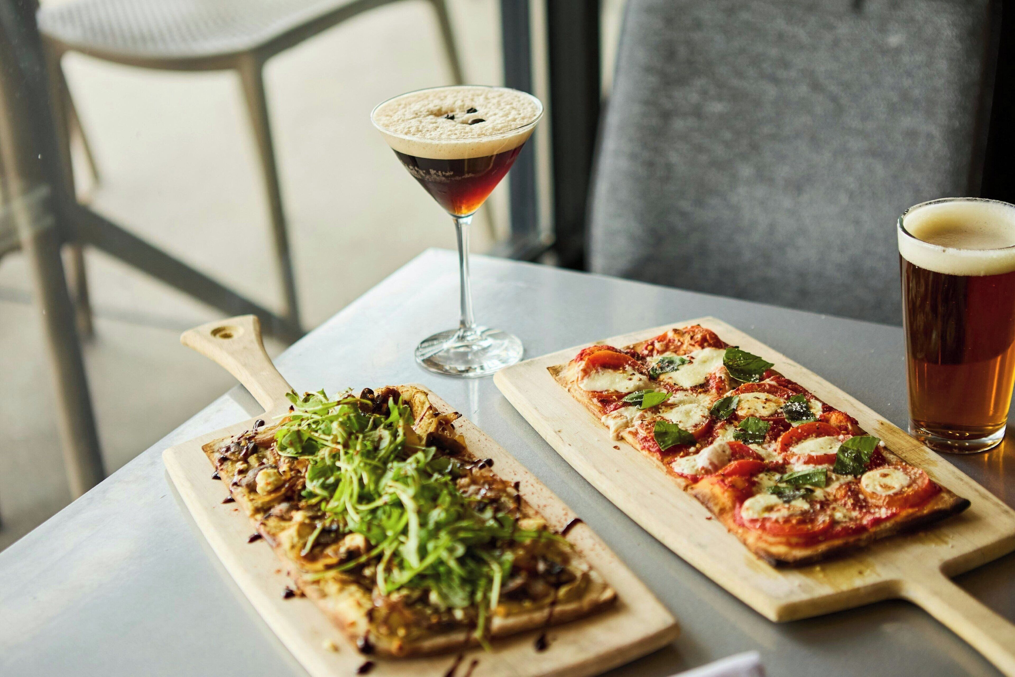 Two pizzas on wooden boards, a martini glass, and a glass of beer on a table.