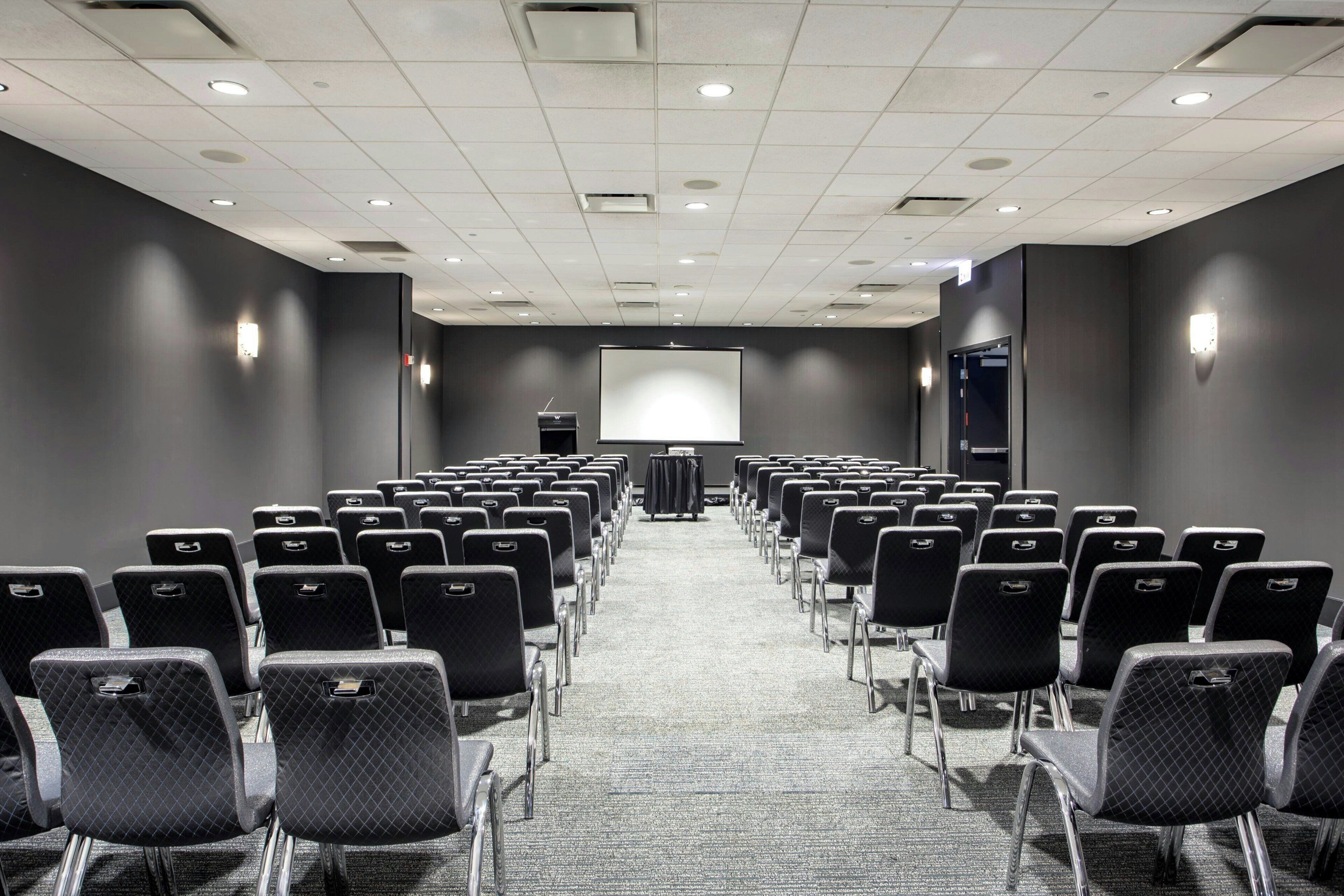 A conference room with rows of chairs, a projector screen, and a podium.