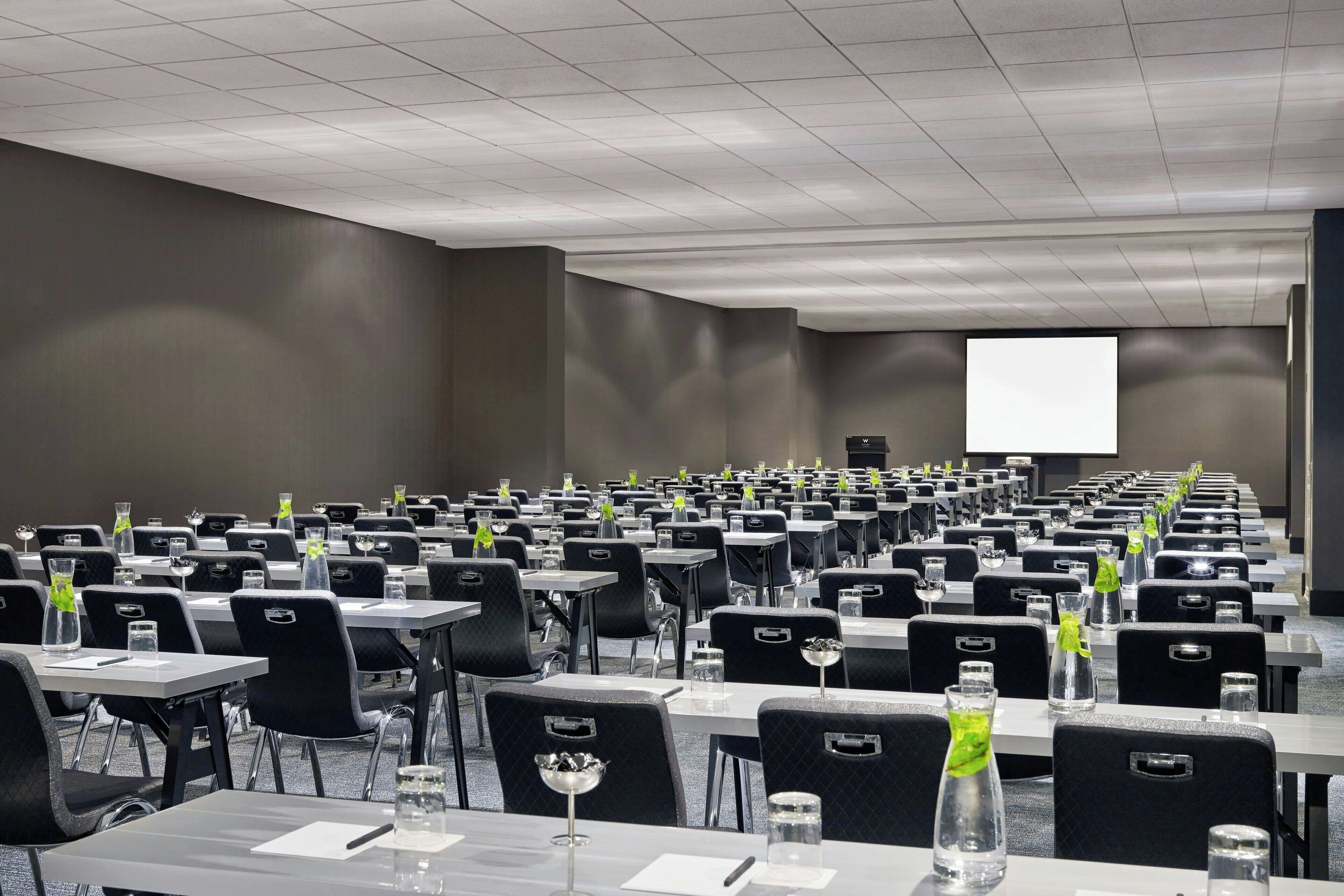 A conference room with rows of tables and chairs, equipped with water bottles and notepads.