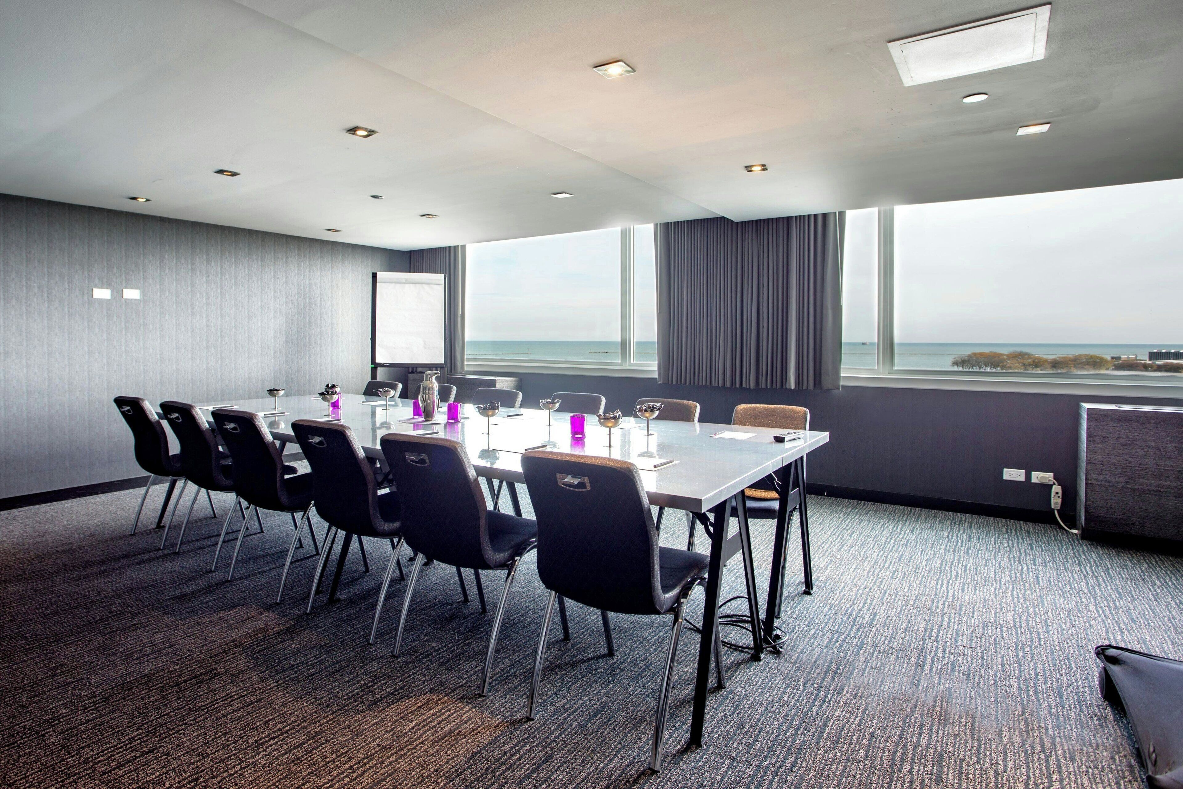 A conference room with a long table, chairs, and a projector screen.