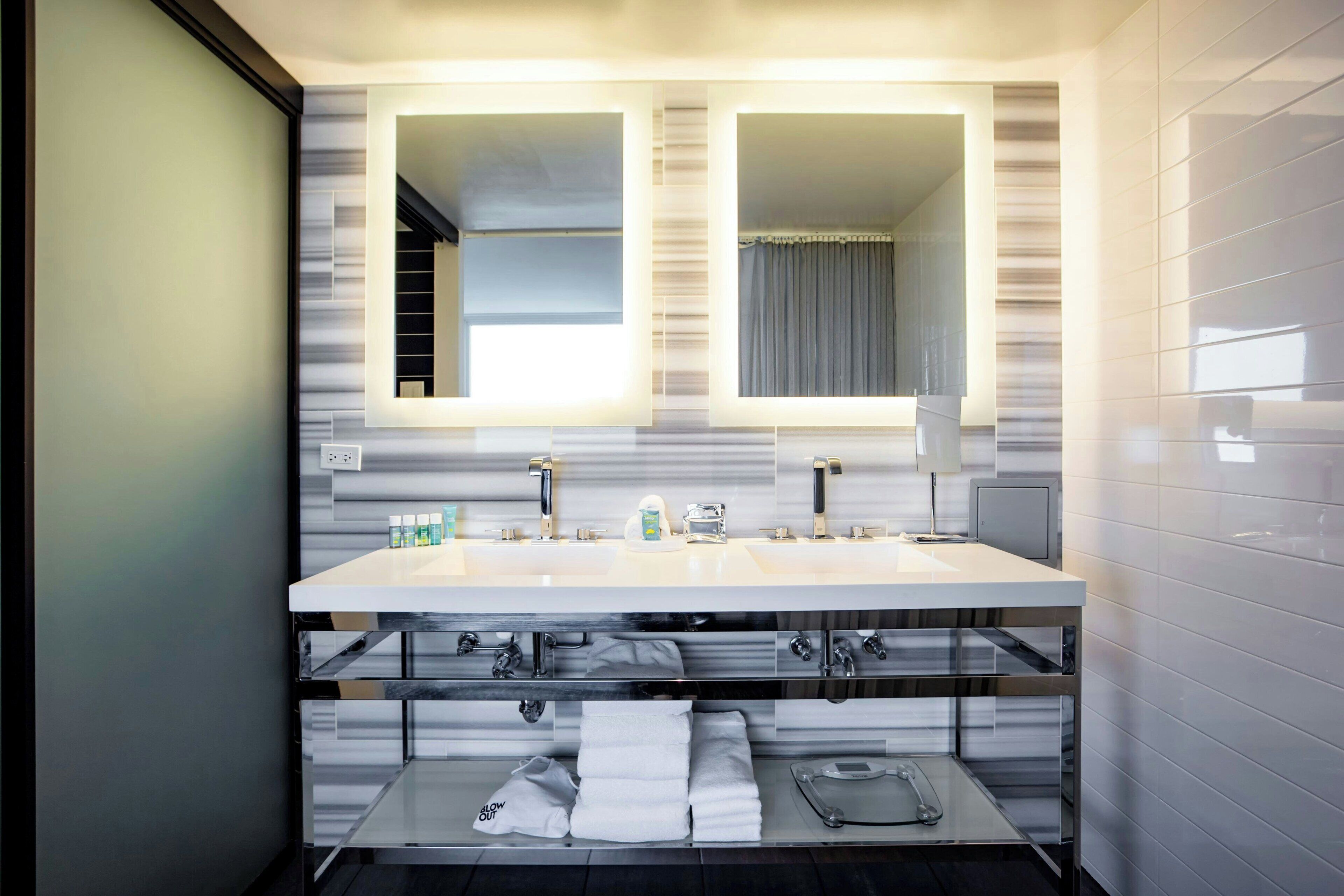 A modern bathroom with a large mirror, two sinks, and a vanity with storage.