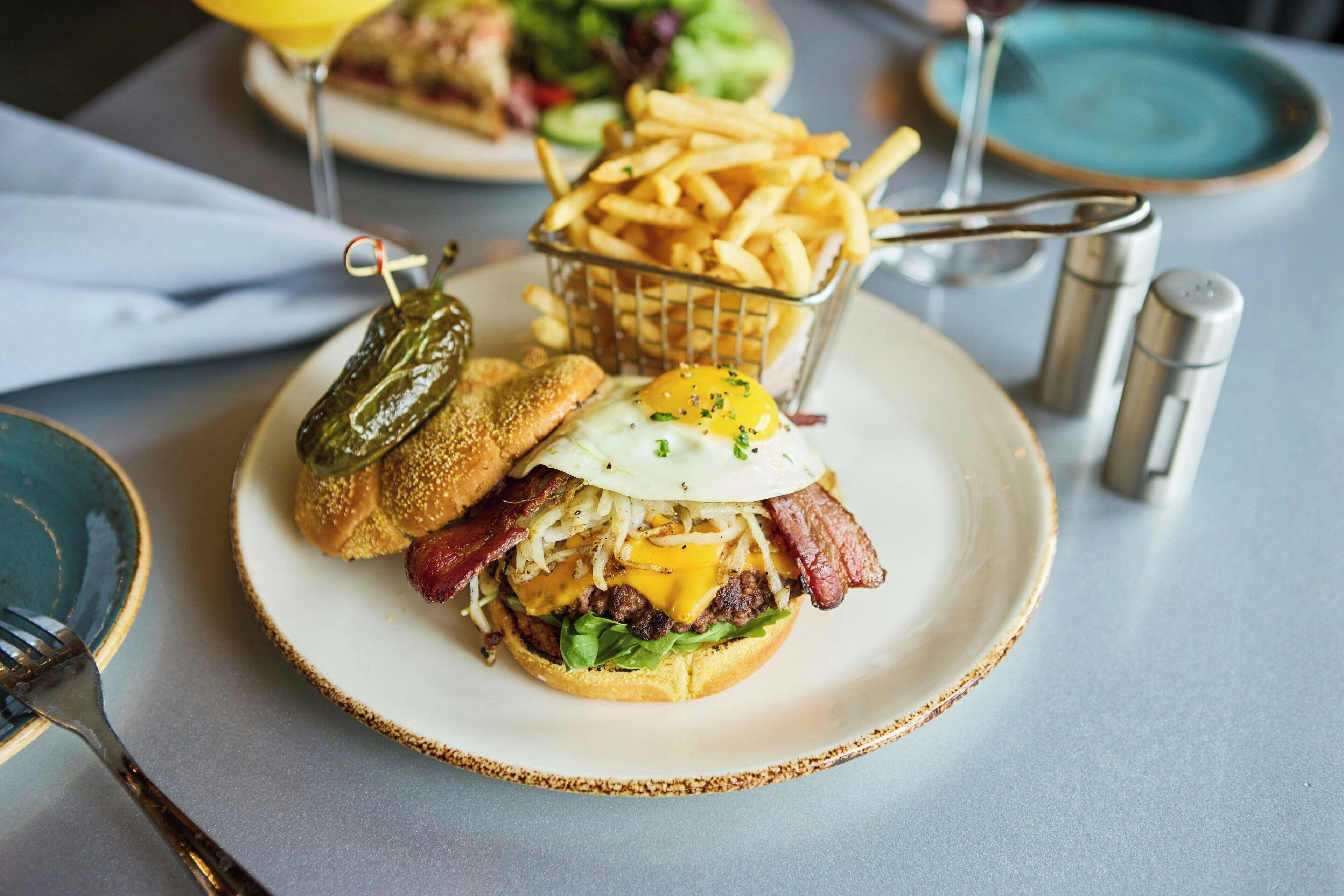 A plate with a burger, fries, and a pickle on a table.