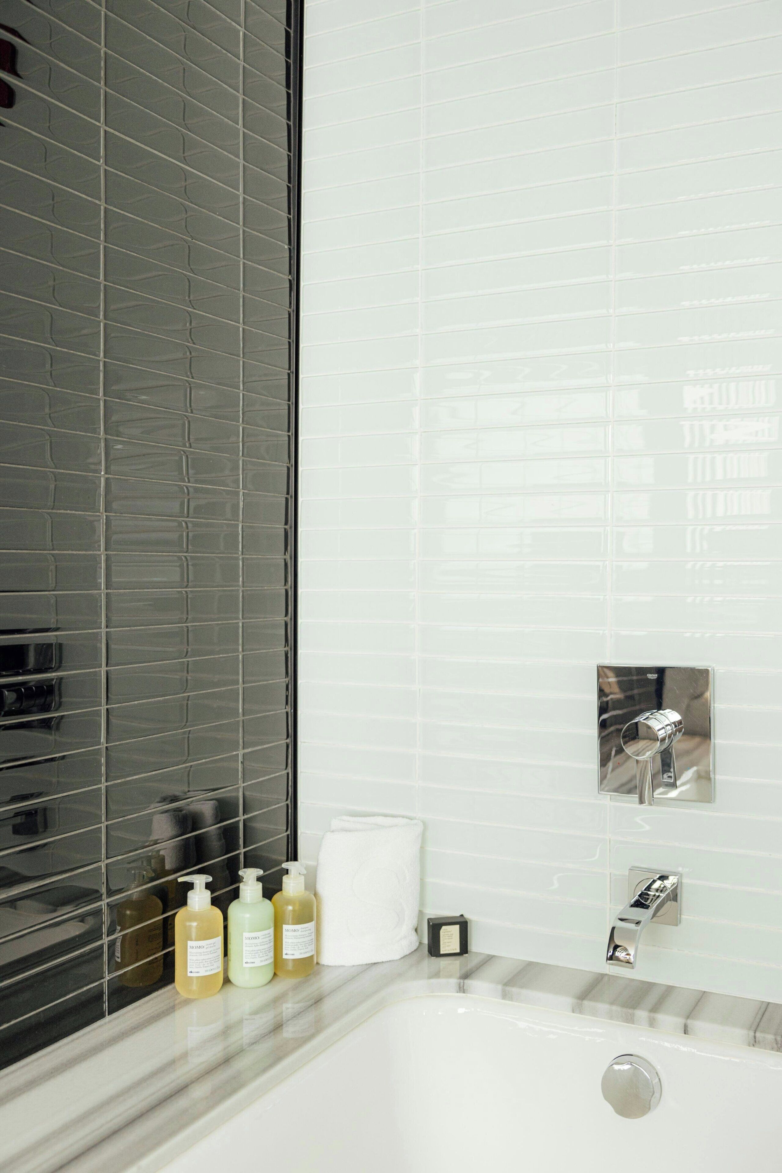 A bathroom with a bathtub, a window with blinds, and toiletries on the counter.