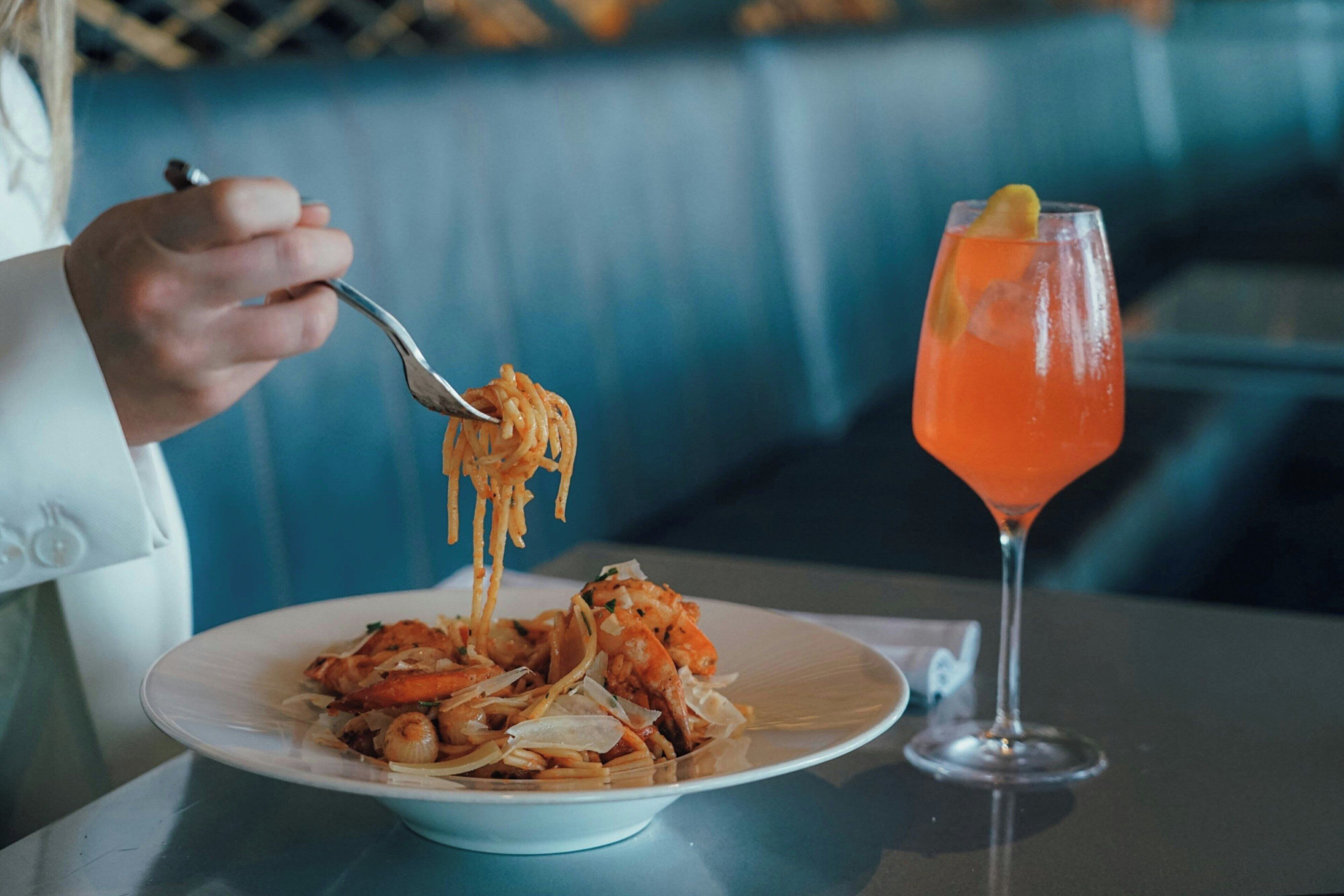 A dining table with a plate of spaghetti and a cocktail glass.