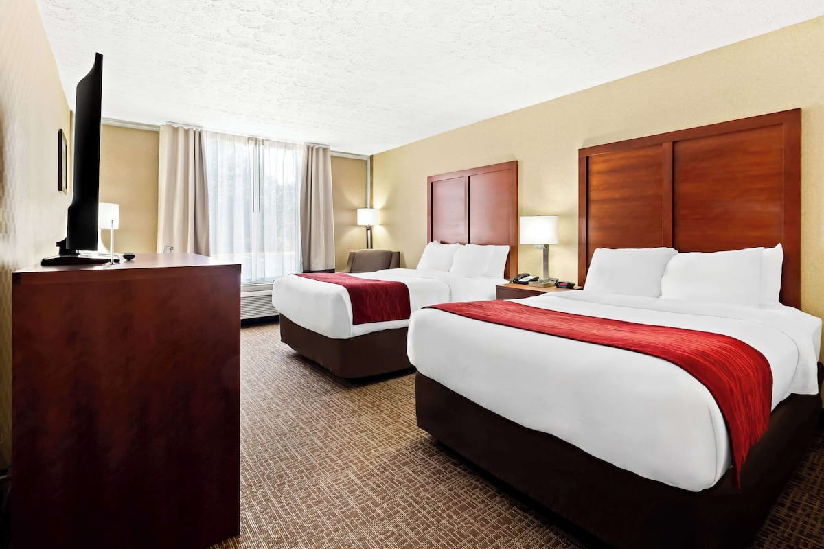 A hotel room with two beds, a desk, a TV, and a window with curtains.