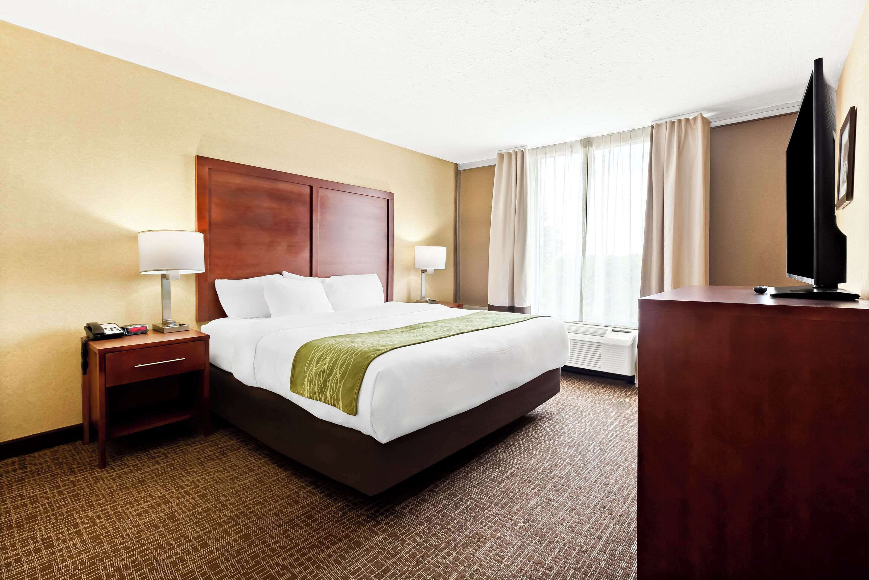 A hotel room with a large bed, bedside tables, a flat-screen TV, and a window with curtains.