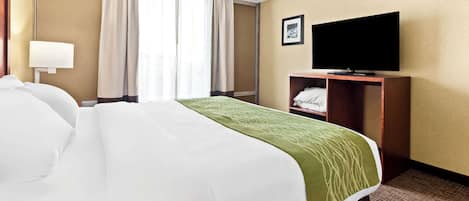 Una habitación de hotel con una cama grande, un televisor sobre un soporte de madera y una ventana con cortinas.