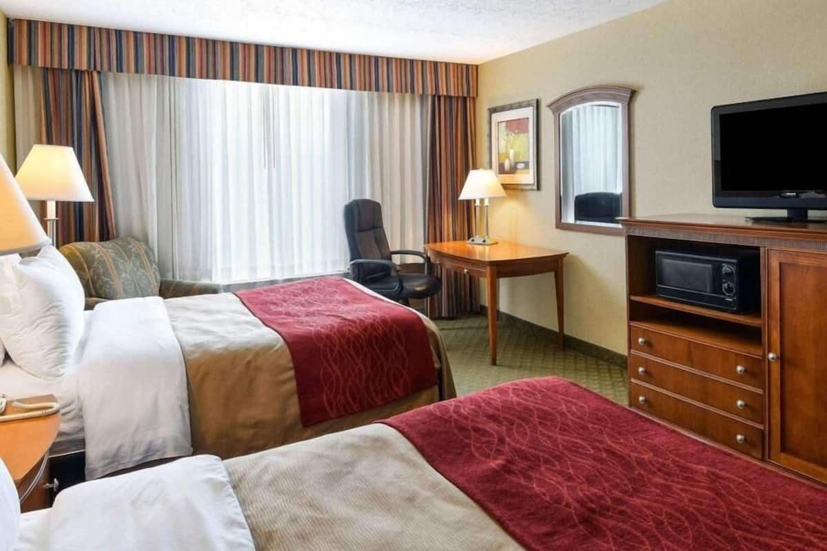 A hotel room with two beds, a desk, a chair, a television, and a dresser.