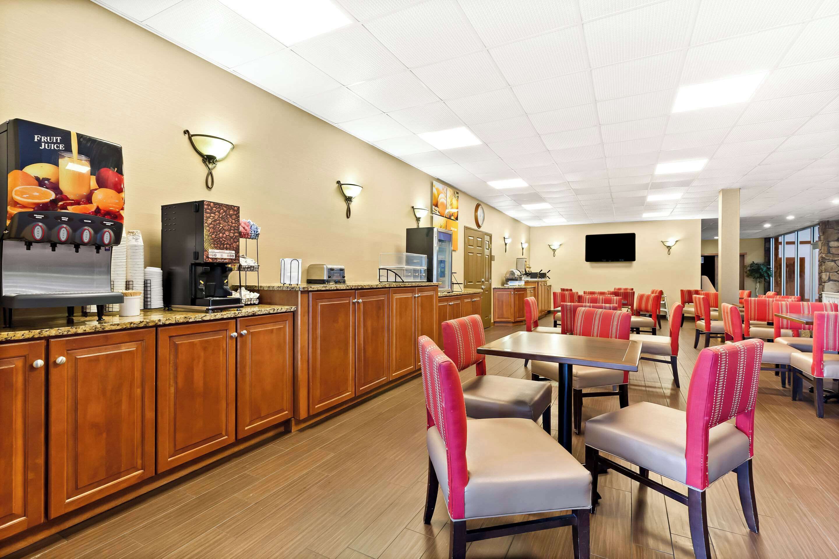 A hotel dining area with wooden cabinets, a fruit juice dispenser, and red and grey chairs.