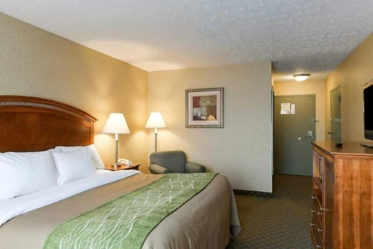 A hotel room with a bed, two bedside lamps, a chair, a dresser, and a framed picture on the wall.