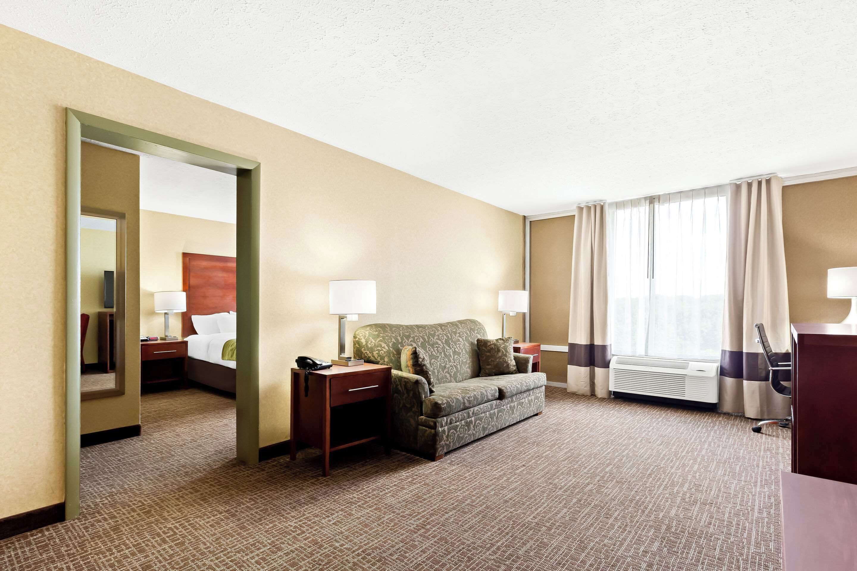 Une chambre d’hôtel équipée d’un lit, d’un bureau, d’une chaise, d’un canapé, d’un miroir et d’une fenêtre avec des rideaux.