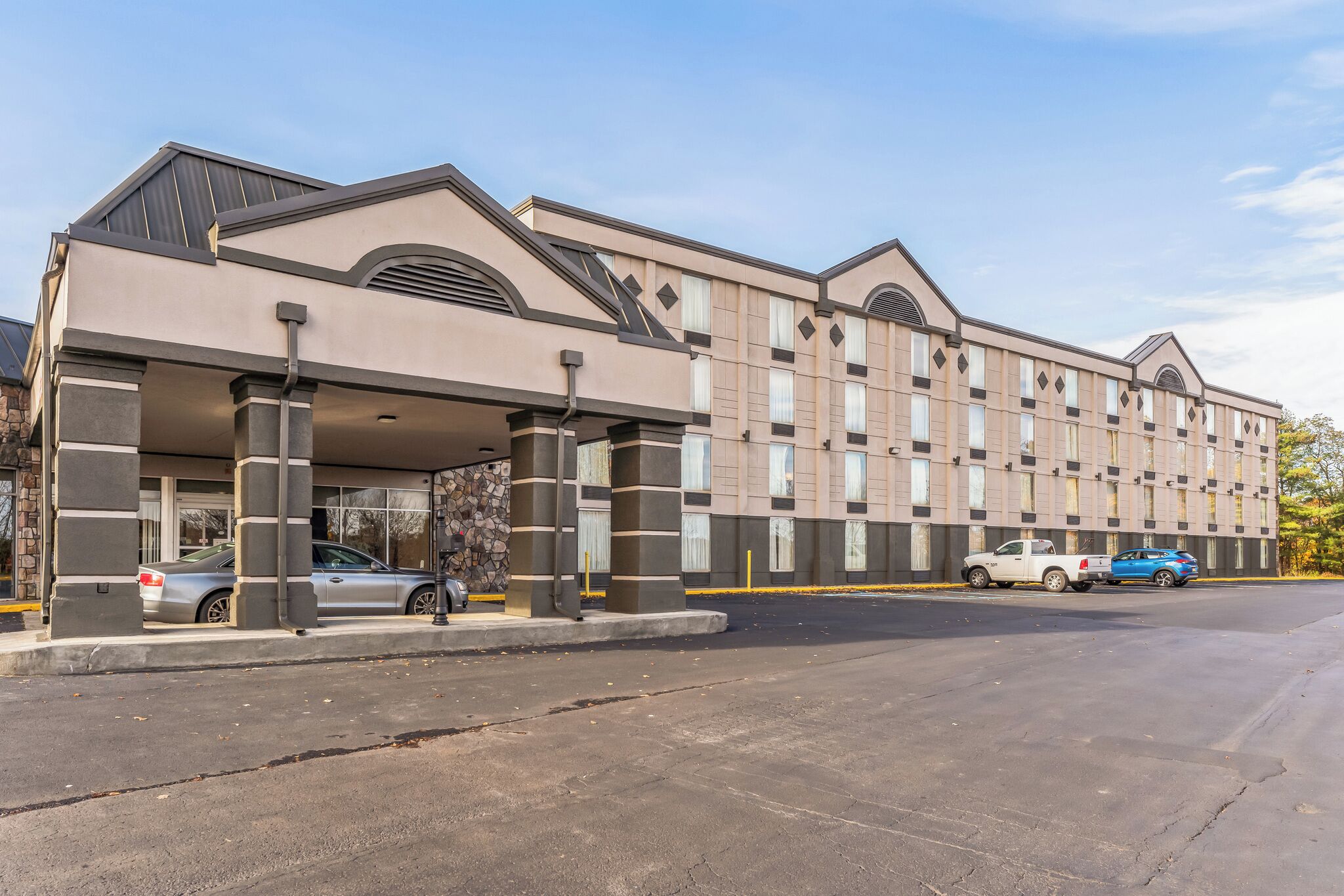 A hotel with a modern facade, a covered entrance, and a parking lot with several cars.