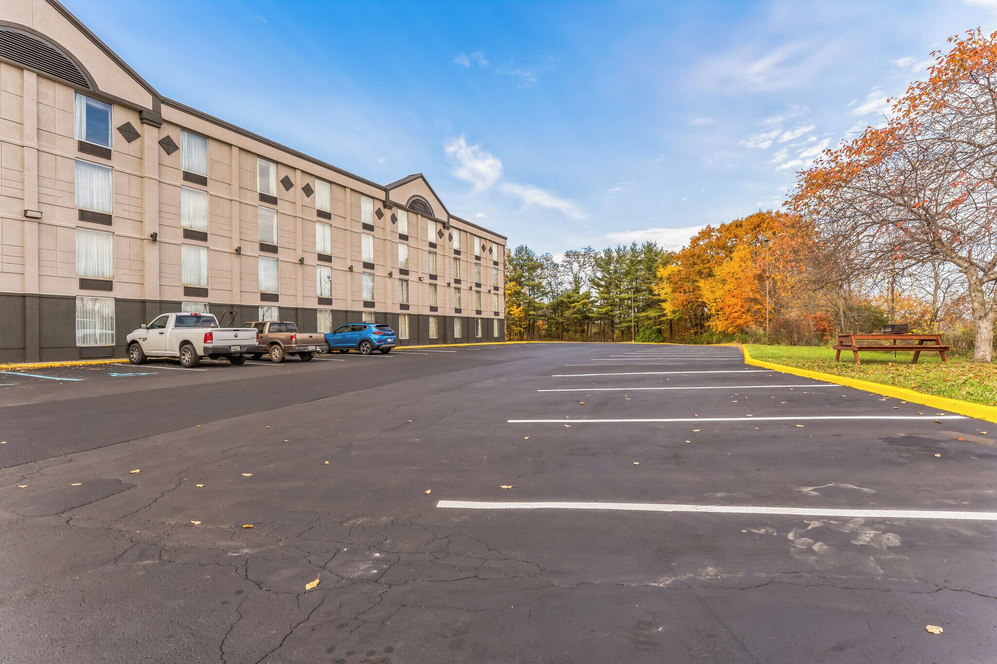 A parking lot with several cars, a building with a beige facade, and autumn trees in the background.