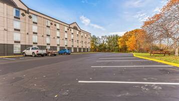 A parking lot with several cars, a building with a beige facade, and autumn trees in the background.